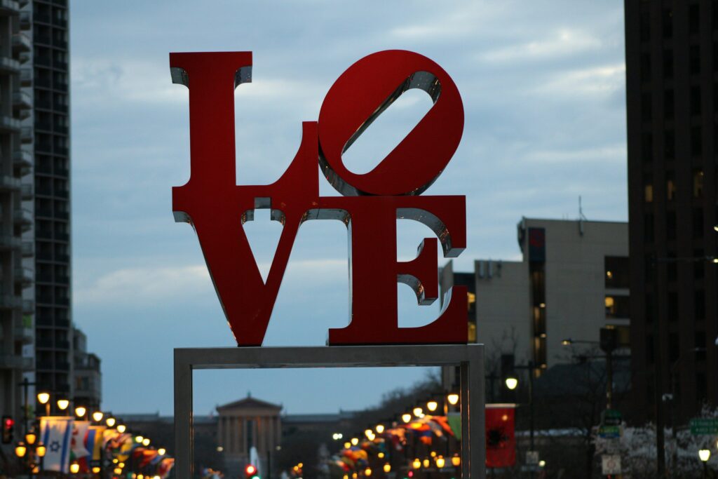 LOVE art sign in Philadelphia's Love Park / JFK Plaza at dusk with streetlights and buildings visible in background.