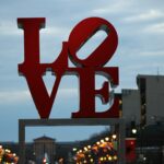 LOVE art sign in Philadelphia's Love Park / JFK Plaza at dusk with streetlights and buildings visible in background.