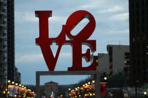 LOVE art sign in Philadelphia's Love Park / JFK Plaza at dusk with streetlights and buildings visible in background.